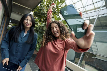 Happy young businesswoman with smart phone by colleague in corridor - JOSEF22579