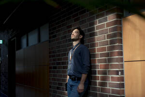 Young businessman with eyes closed standing in front of brick wall - JOSEF22612