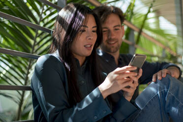 Businesswoman sharing mobile phone with colleague in corridor - JOSEF22646