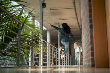 Businesswoman jumping in corridor at office - JOSEF22658