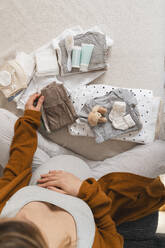 Pregnant woman packing baby clothes at home - NDEF01496