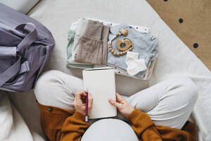 Pregnant woman preparing checklist with diary at home - NDEF01499