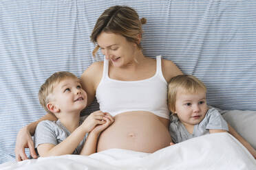 Lächelnde schwangere Mutter umarmt Kinder auf dem Bett zu Hause - NDEF01501