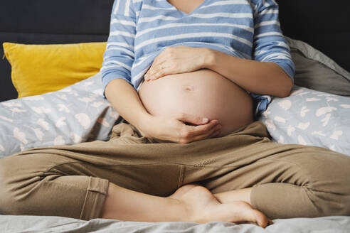 Schwangere Frau sitzt zu Hause auf dem Bett - NDEF01506