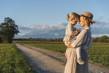 Schwangere Mutter umarmt Tochter in der Nähe Feld bei Sonnenuntergang - NDEF01515