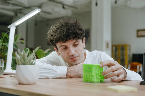 Smiling businessman playing with cube maze in office - YTF01564