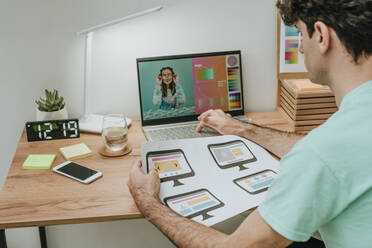 Webdesigner hält ein Dokument und arbeitet an einem Laptop im Büro - YTF01580