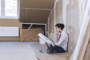 Young woman reading blueprint for home development - UUF30884