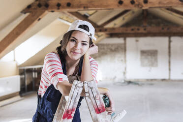 Smiling woman leaning on ladder at home - UUF30887