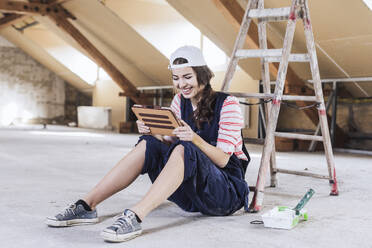 Smiling woman using tablet PC near ladder at home - UUF30888