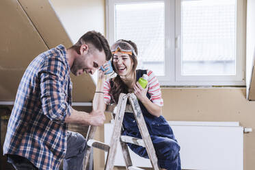 Cheerful couple laughing near ladder at home - UUF30891