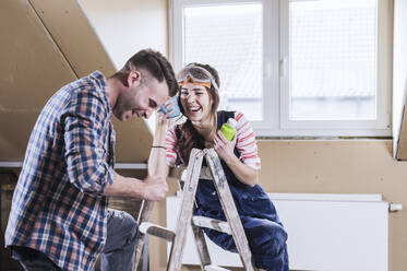 Fröhliches Paar lachend in der Nähe der Leiter zu Hause - UUF30891