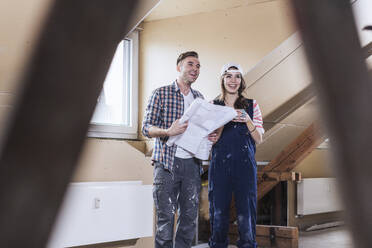 Smiling couple holding blueprint at home - UUF30893