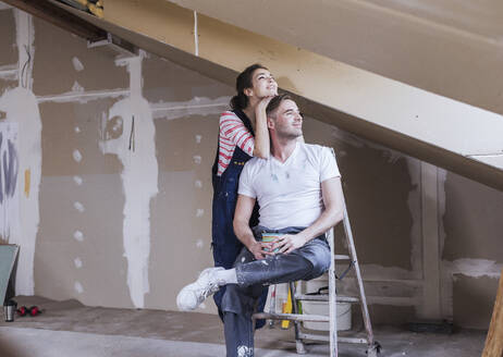 Lächelnder Mann, der auf einer Leiter sitzt, mit einer Frau, die zu Hause steht - UUF30897