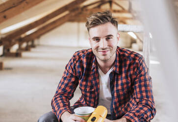 Smiling man with coffee mug and electric drill at home - UUF30898