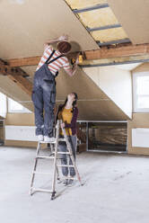 Man standing on ladder and drilling wall with woman at home - UUF30899