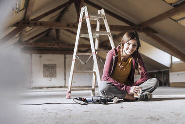 Young woman having coffee near ladder at home - UUF30905