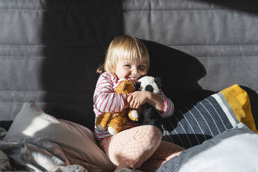 Fröhliches Mädchen umarmt Plüschtiere auf dem Bett zu Hause - NDEF01517