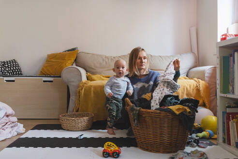 Mutter sitzt in der Nähe von Wäschekorb mit Sohn spielen zu Hause - NDEF01544