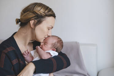 Mother kissing and embracing baby boy in front of wall at home - NDEF01547