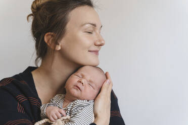 Lächelnde Mutter umarmt kleinen Jungen vor einer weißen Wand - NDEF01550