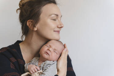 Smiling mother embracing baby boy in front of white wall - NDEF01550