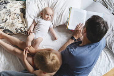 Vater liest mit Kindern auf dem Bett zu Hause ein Buch - NDEF01551