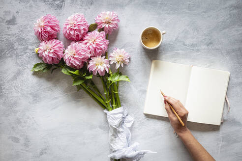 Tagebuch schreibende Frauenhand vor einem Strauß rosa blühender 