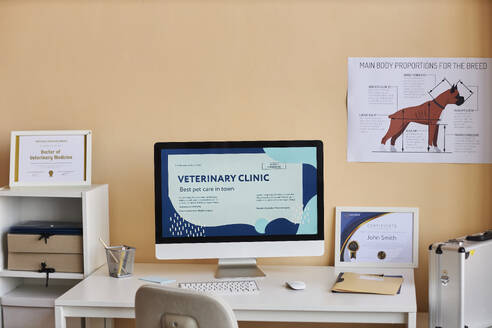 Computer on desk near certificates and dog diagram in veterinary clinic - KPEF00519