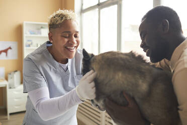 Happy veterinarian petting dog with owner in clinic - KPEF00553