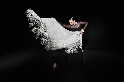 Young flamenco dancer performing with shawl against black background - MRRF02739