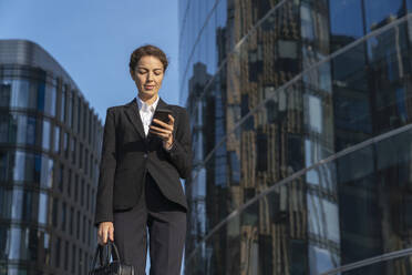 Geschäftsfrau benutzt Smartphone in der Nähe von Gebäuden in der Stadt - VPIF09201