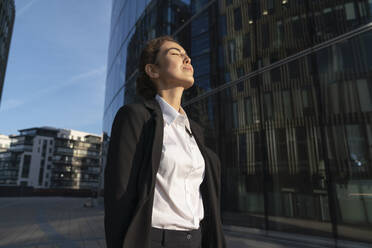 Geschäftsfrau steht mit geschlossenen Augen in der Nähe eines Gebäudes in der Stadt - VPIF09208