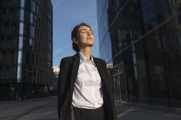 Businesswoman wearing blazer and standing with eyes closed in city - VPIF09210