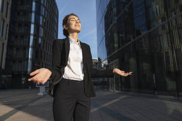 Smiling businesswoman standing with arms raised near buildings - VPIF09211