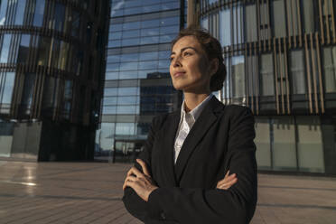 Thoughtful businesswoman standing with arms crossed at sunset - VPIF09212