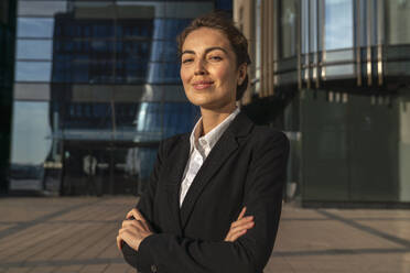 Smiling young businesswoman standing with arms crossed in front of building - VPIF09214