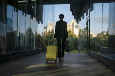 Businesswoman pulling suitcase amidst glass wall - VPIF09215