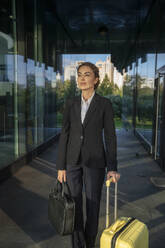 Thoughtful businesswoman standing with suitcase and briefcase - VPIF09216