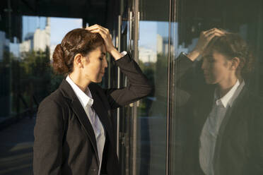 Frustrierte Geschäftsfrau lehnt an einer Glaswand - VPIF09220
