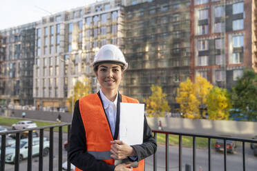 Lächelnder Ingenieur, der einen Aktenordner hält und auf dem Balkon steht - VPIF09225