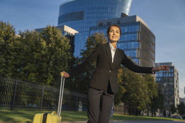 Smiling businesswoman standing with suitcase and hailing ride in city - VPIF09232