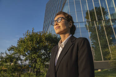 Contemplative businesswoman standing in front of building in office park - VPIF09235