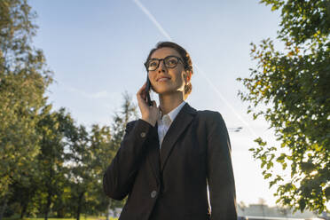 Smiling businesswoman talking on smart phone in park - VPIF09241