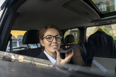 Lächelnde Geschäftsfrau, die ihre Mailbox auf einem Smartphone im Auto aufnimmt - VPIF09250