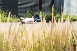 Geschäftsmann entspannt sich in der Nähe eines Gebäudes an einem sonnigen Tag - UUF30914