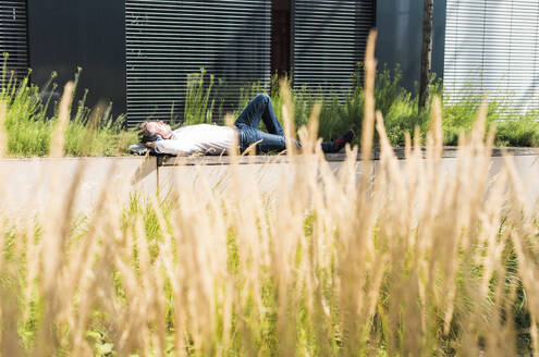 Businessman relaxing near building on sunny day - UUF30914