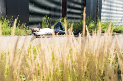 Geschäftsmann entspannt sich in der Nähe eines Gebäudes an einem sonnigen Tag - UUF30914