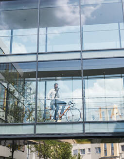 Geschäftsmann sitzt auf einem Fahrrad und sendet eine Voicemail über ein Smartphone im Büro - UUF30925