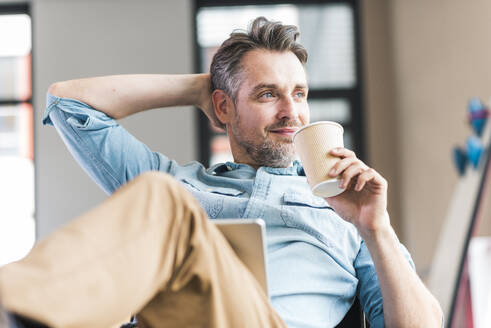 Lächelnder Geschäftsmann hält Einweg-Kaffeebecher im Büro - UUF30930